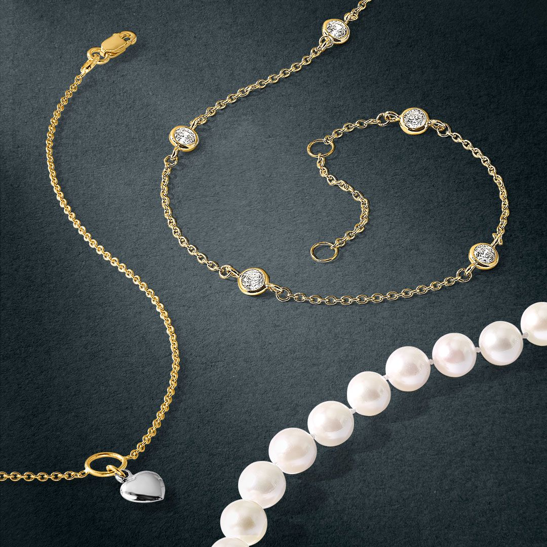 3 necklaces spread across a table. One with a heart pendant in the middle, another with 5 diamonds spaced around the necklace, and another pearl necklace.
